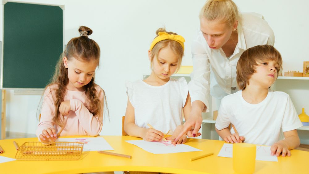 Teacher helping two children make colorful paper crafts