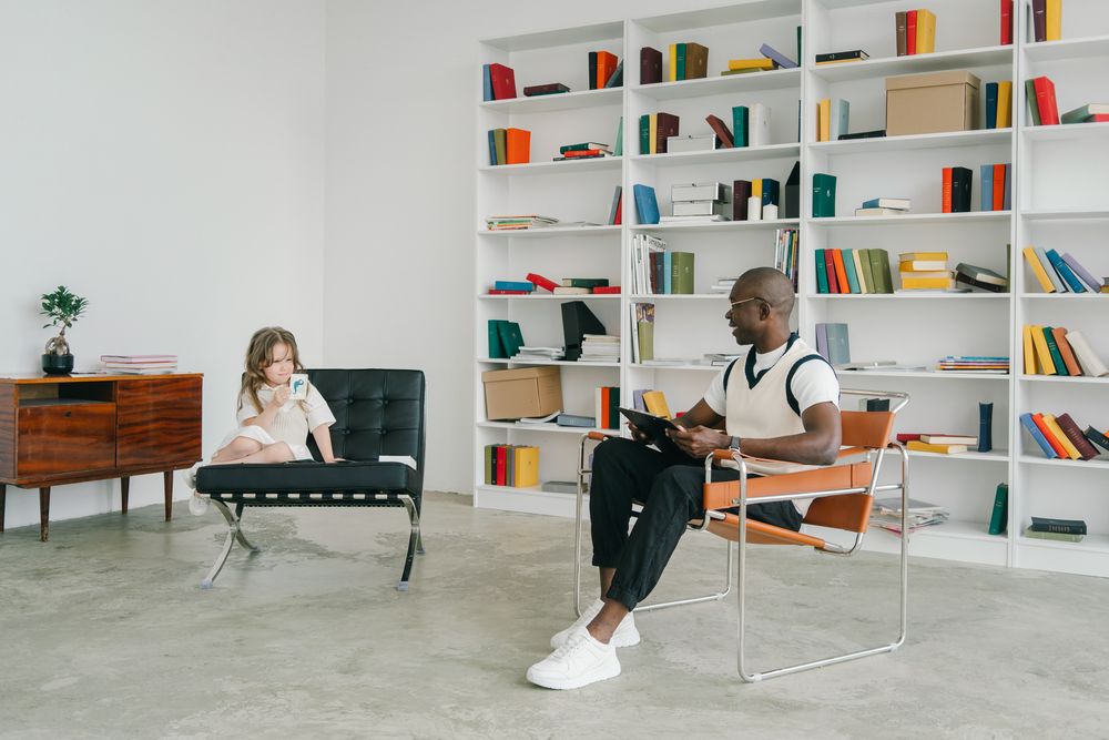 Black teacher listening to a young child seated beside him in the classroom